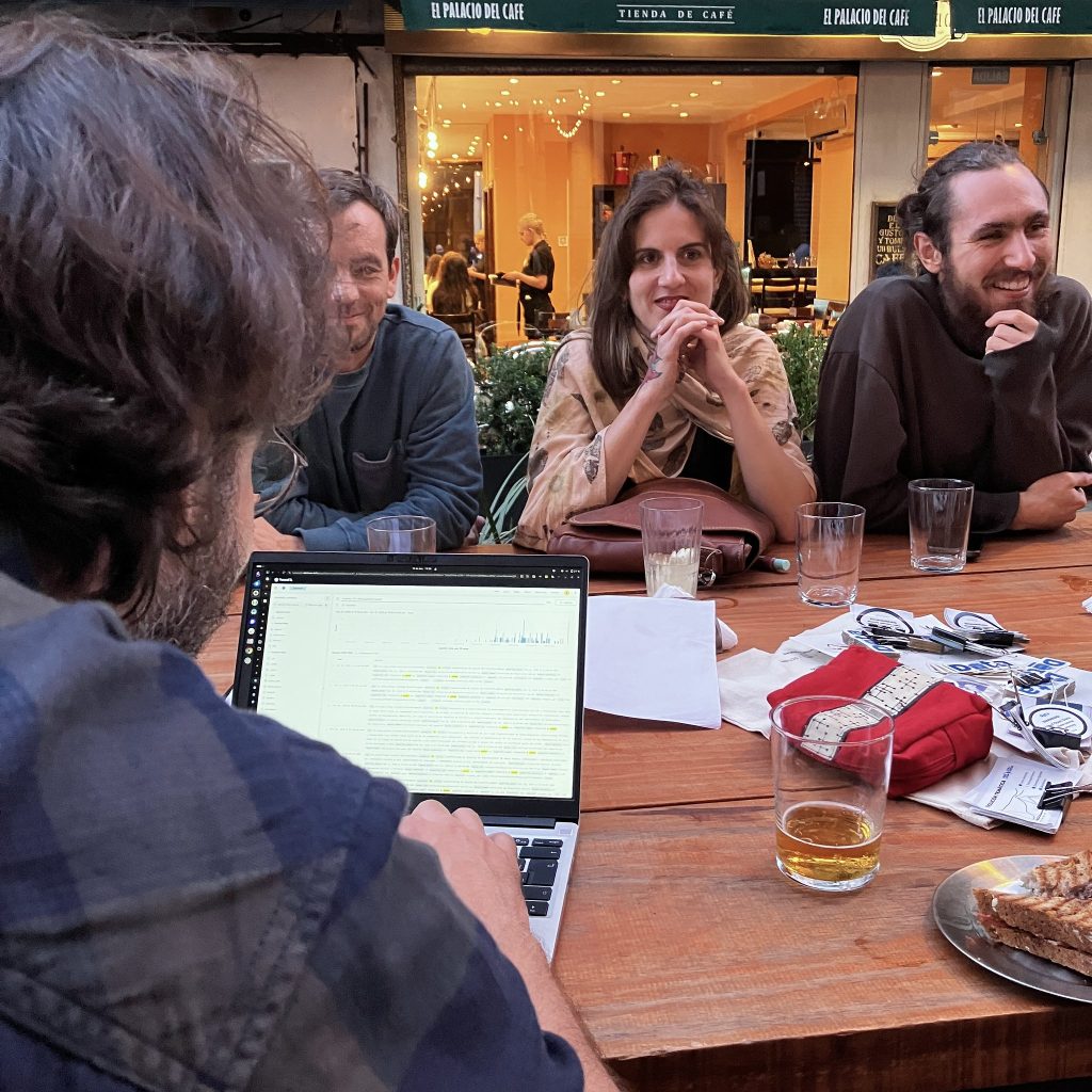 Vista de atrás de persona trabajndo en su computadora una visualización, mientras del otro lado de la mesa escuchan la presentacion de alguien más.